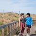 A couple in activewear strolling together on a sunny boardwalk in a natural setting.